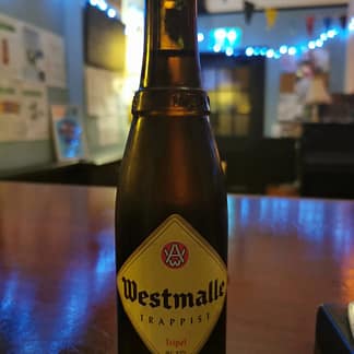 Brown bottle with a yellow diamond label reading Westmalle sits on a polished wooden surface
