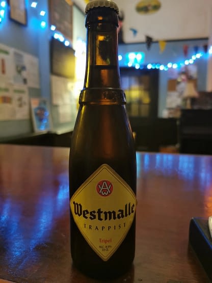 Brown bottle with a yellow diamond label reading Westmalle sits on a polished wooden surface