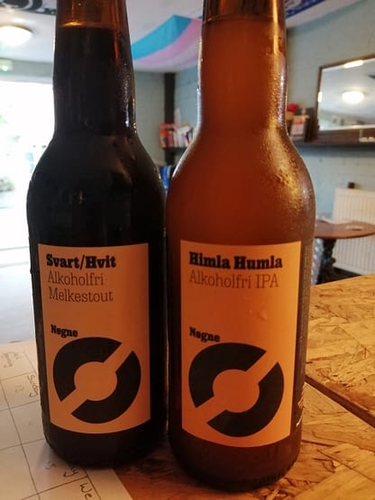 A pair of brown bottles side by side, one is filled with a darker liquid than the other both have orange labels